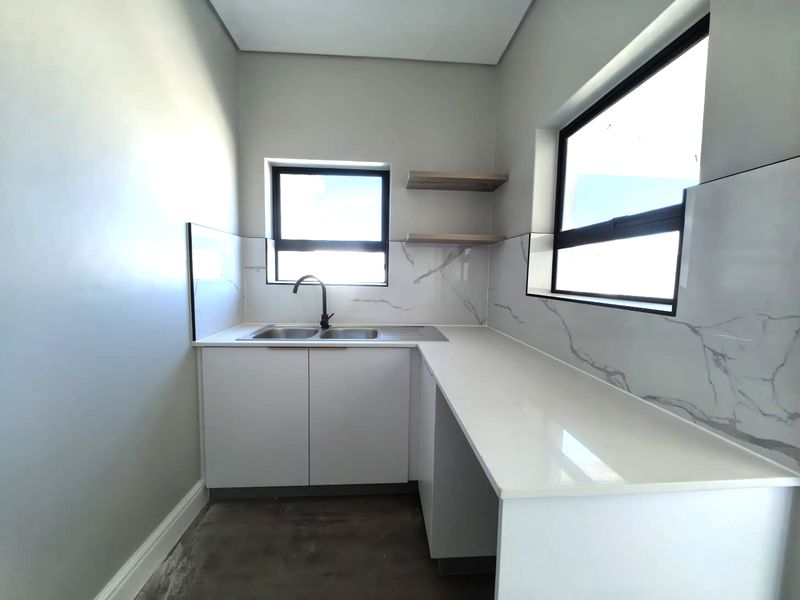 A modern scullery featuring white cabinetry, stone-look countertops, marble-effect splashback tiling, a double sink with a black mixer tap, and floating timber shelves.