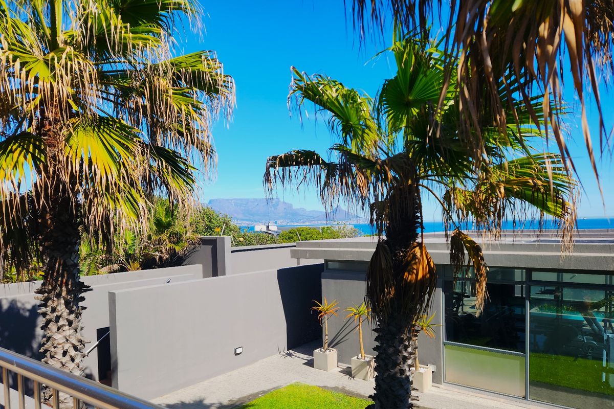 A view of the property exterior featuring modern grey walls, landscaped garden area, and a scenic backdrop of Table Mountain and the ocean.