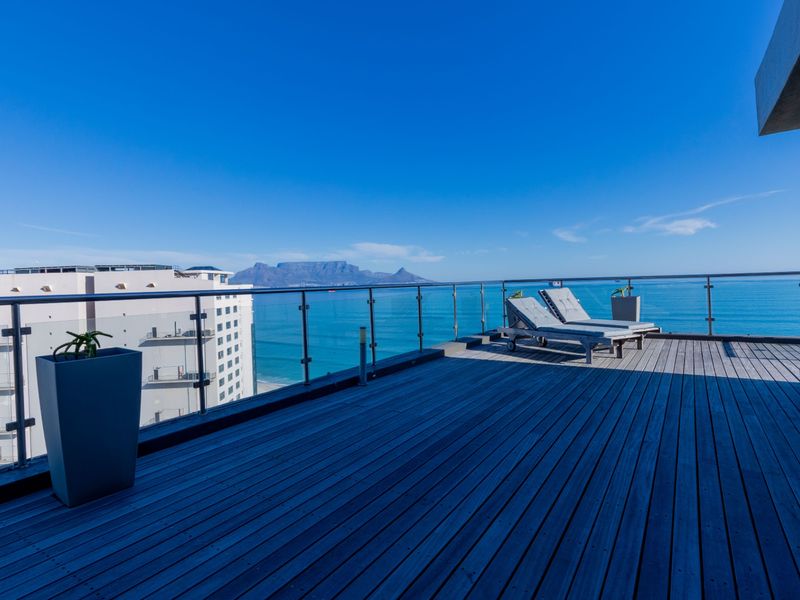 Spacious balcony featuring timber decking and a modern glass balustrade, offering panoramic ocean and mountain views.