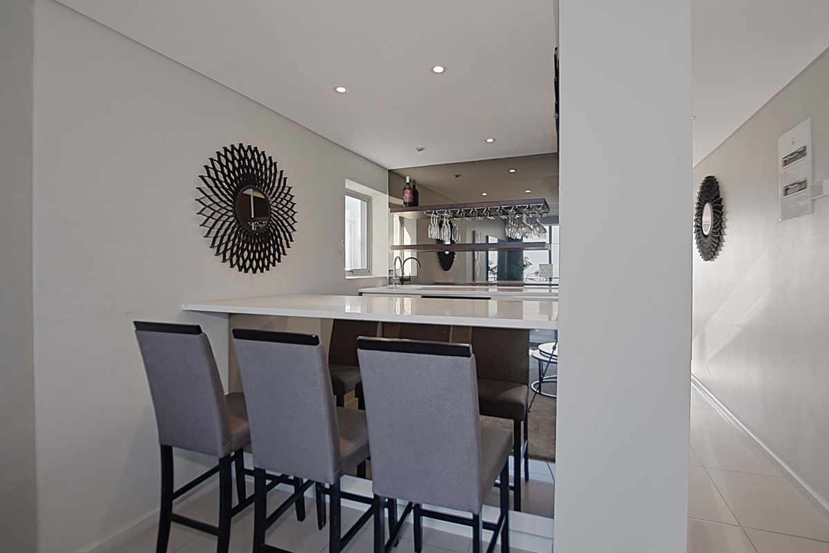 A modern kitchen area featuring a sleek breakfast bar with stone countertop, integrated shelving, and recessed downlighting.