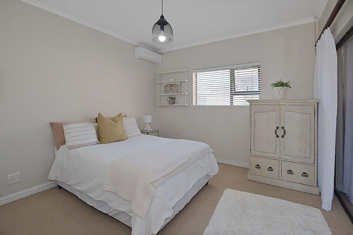 A well-lit bedroom featuring neutral walls, carpeted flooring, a wall-mounted air conditioning unit, and sliding glass doors providing access to the exterior.