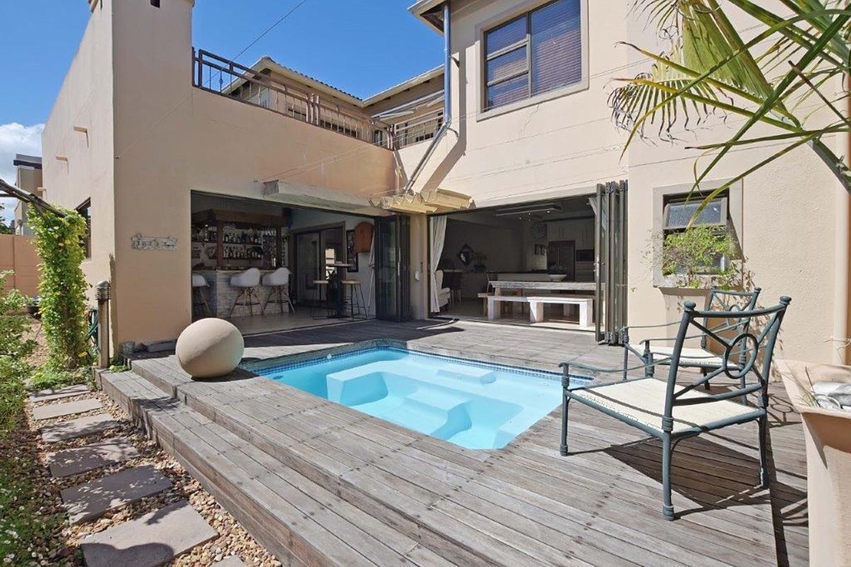 Rear exterior view featuring a built-in swimming pool, timber decking, and seamless indoor-outdoor flow through large folding doors into the living and bar area.