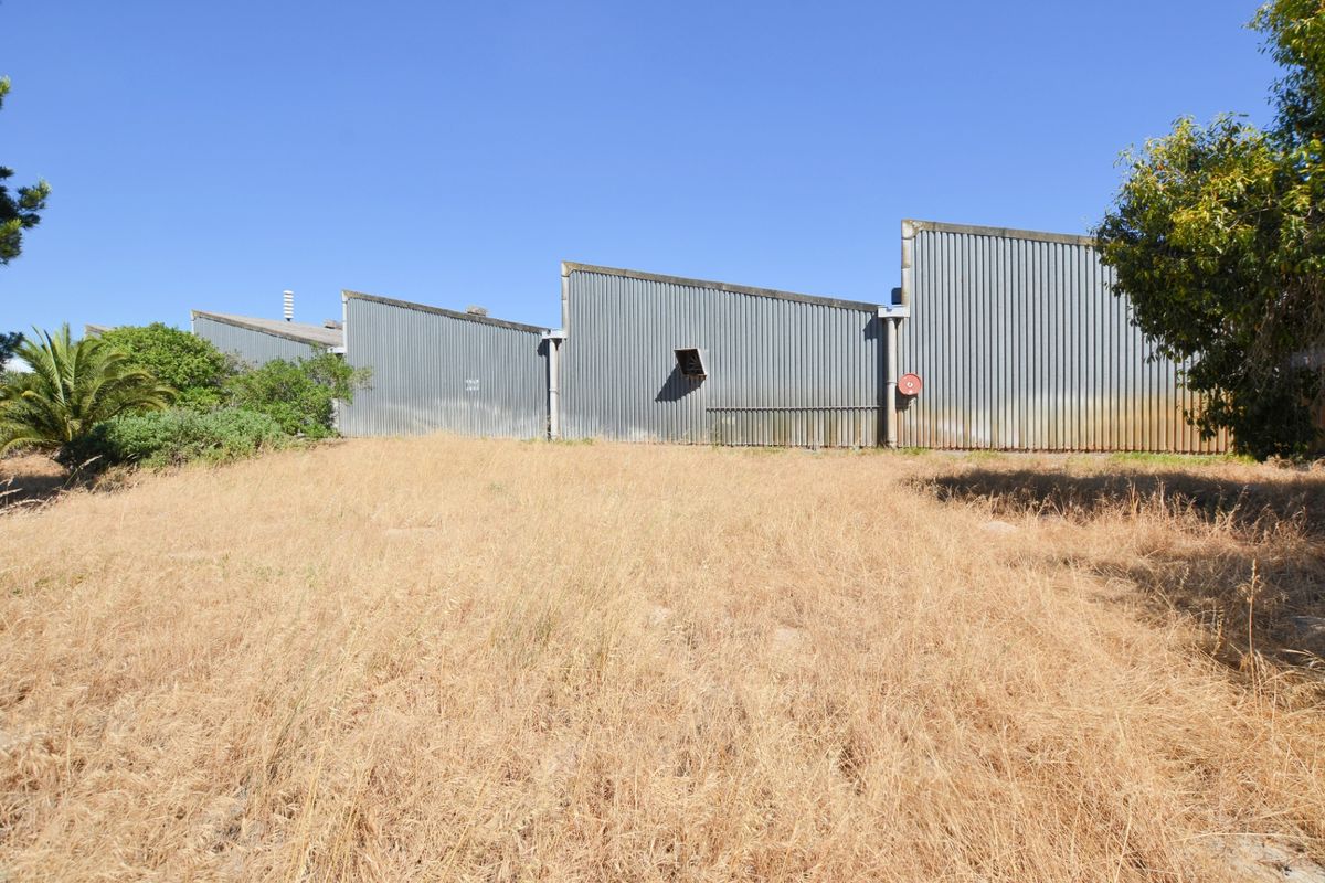 Rear view of an industrial warehouse building featuring corrugated metal cladding and a large, unmaintained grass area.