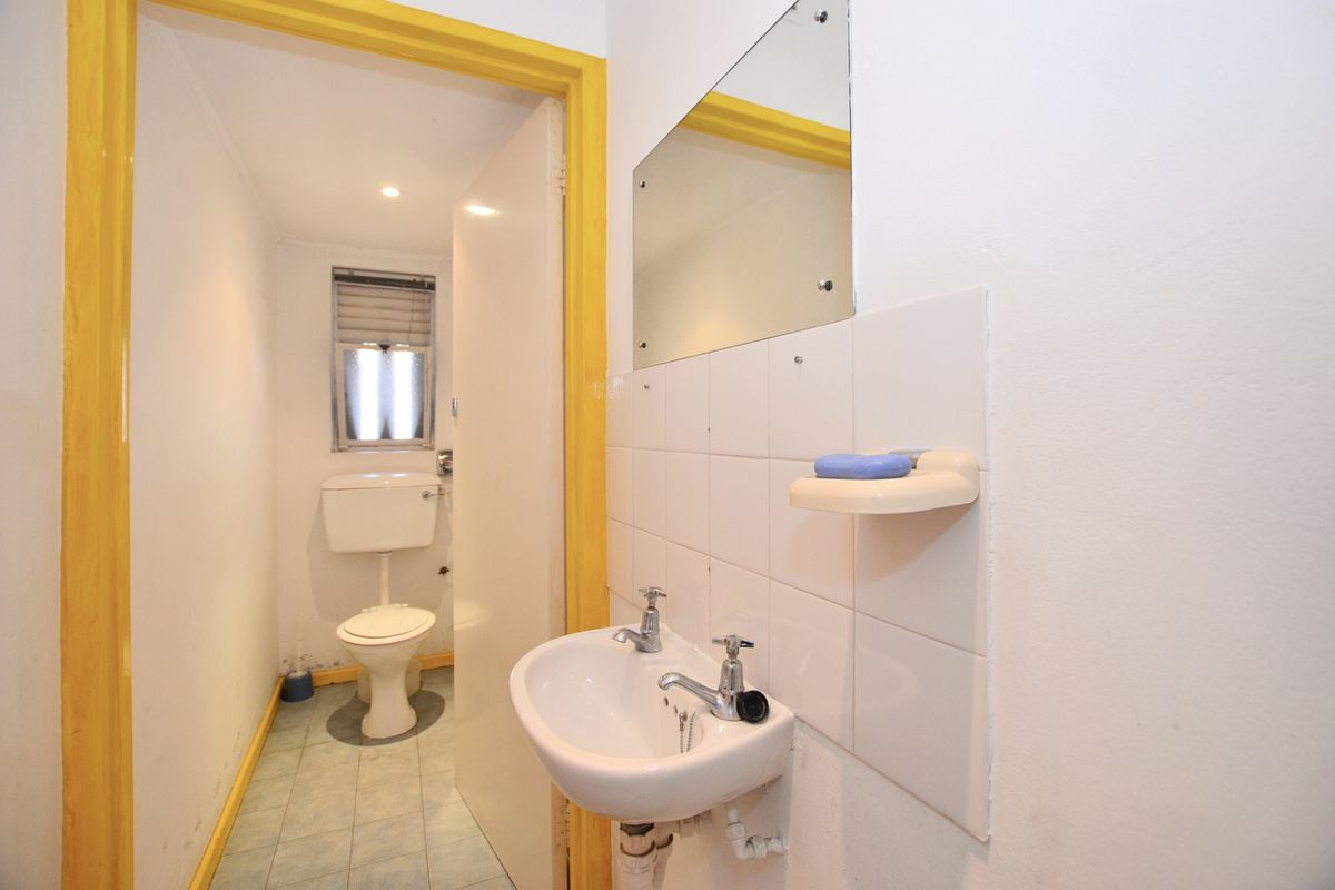 A functional bathroom featuring a wall-mounted basin, tiled splashback, mirror, and a separate toilet area with a window.