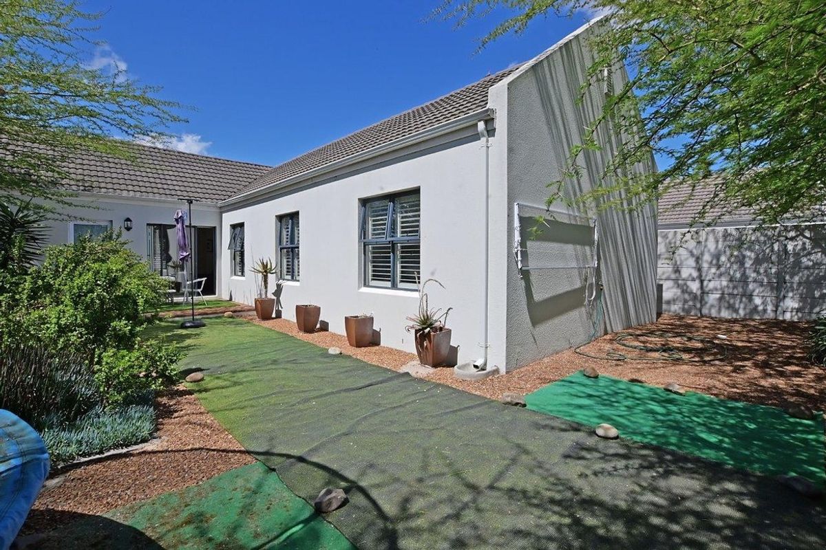 Rear view of the house featuring a paved and artificial turf garden area with established landscaping and exterior wall-mounted drying rack.