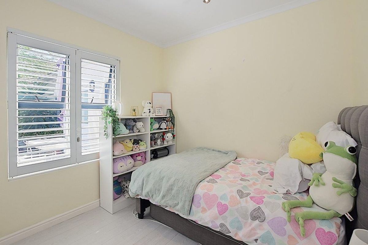 A bedroom featuring light-toned flooring, neutral walls, and white plantation shutters on the window.