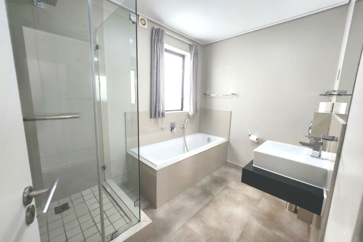 Modern bathroom featuring a glass-enclosed shower, a built-in bathtub, and a contemporary wall-mounted vanity basin with neutral floor tiling.