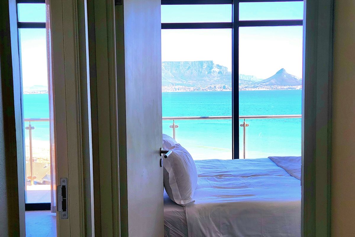 A bedroom featuring floor-to-ceiling windows with expansive ocean and mountain views, including a private balcony access.