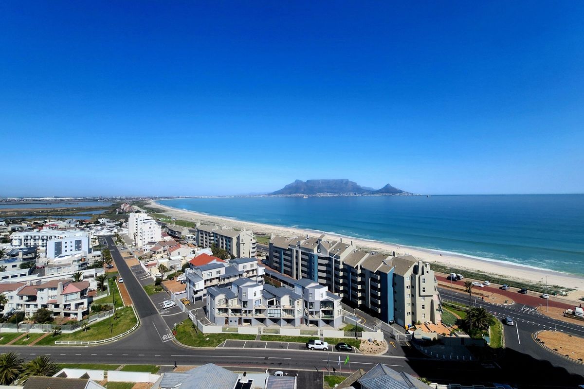 Panoramic aerial view overlooking the coastline, residential apartment complexes, and Table Mountain in the distance.