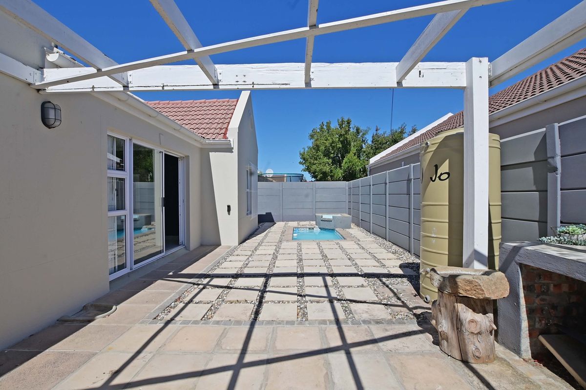 A private rear courtyard featuring a paved patio area, a small plunge pool, and a built-in water storage tank under a timber pergola structure.