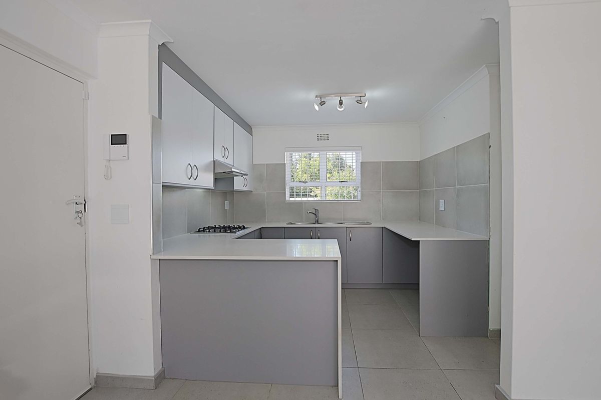 A modern, U-shaped kitchen featuring grey cabinetry, white countertops, a built-in gas hob, extractor fan, and tiled flooring.