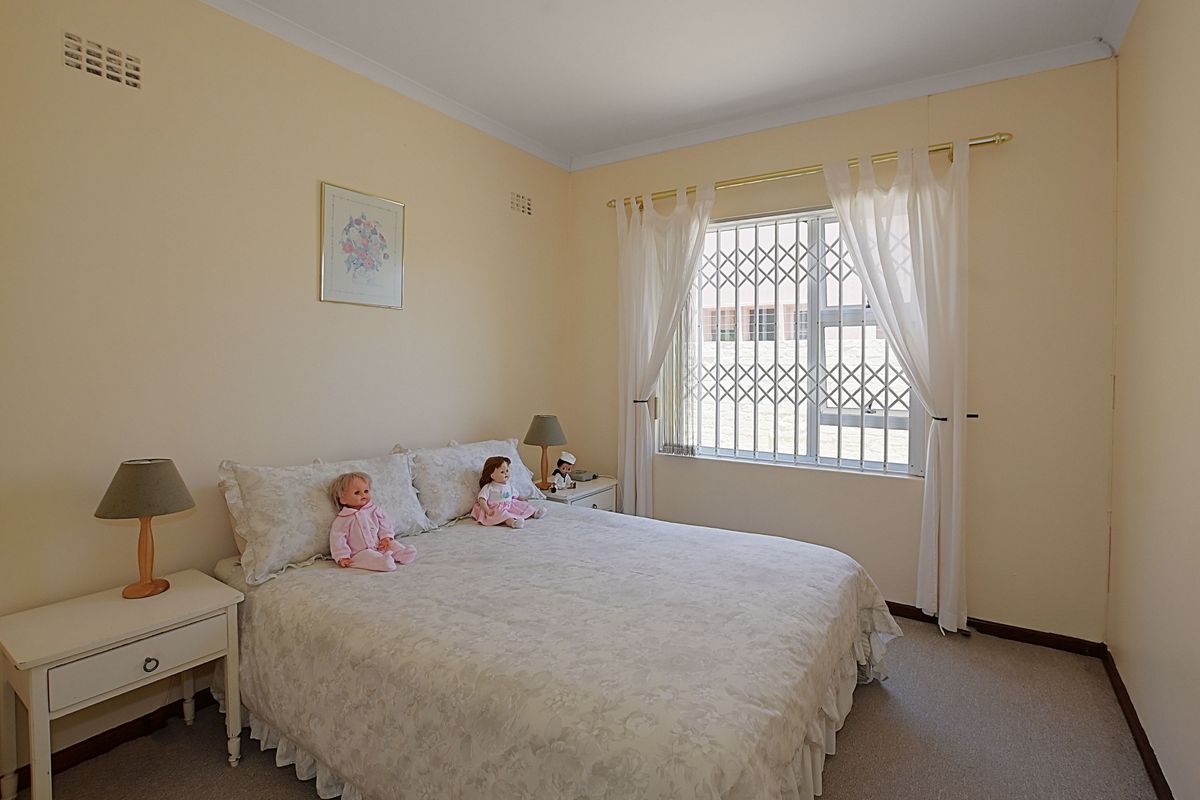 A standard bedroom featuring neutral wall tones, carpeted flooring, and a window fitted with a security gate.