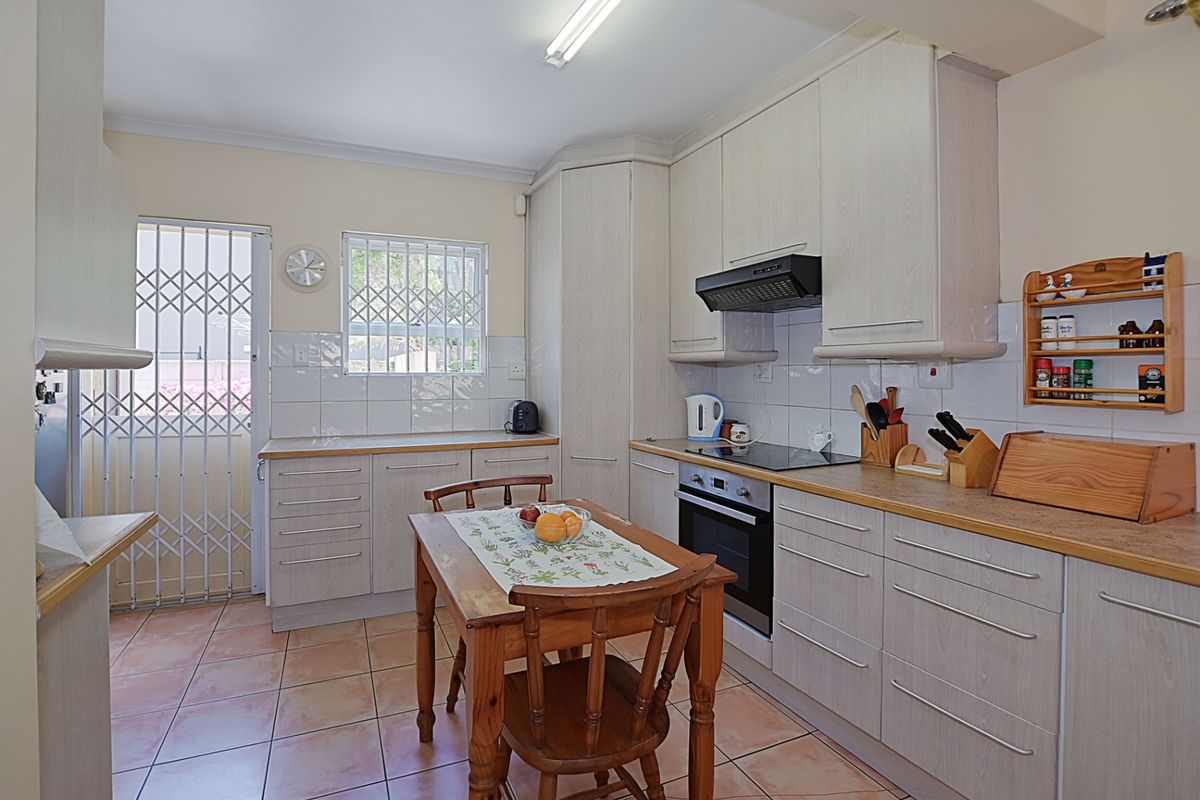 Functional kitchen featuring light-toned cabinetry, tiled flooring, built-in oven, hob, and extractor fan, with direct access to an exterior security gate.