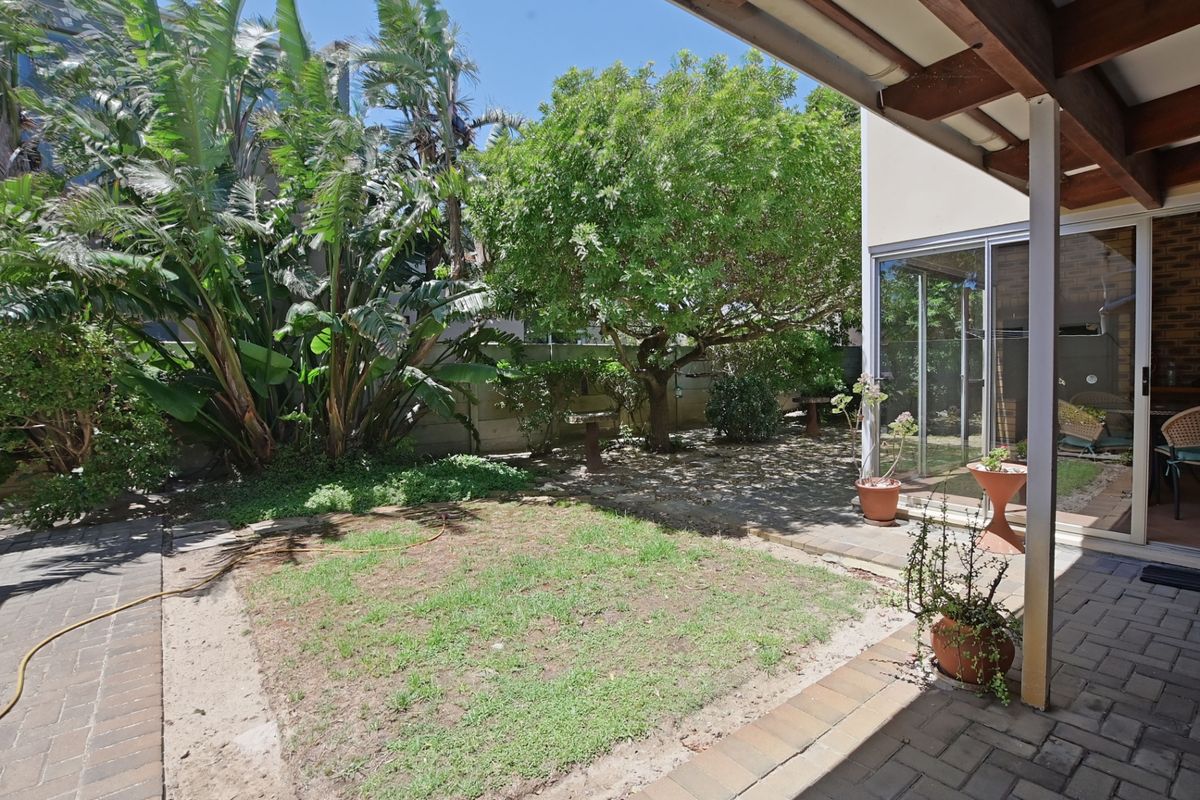 A private rear garden featuring a paved patio area, established trees, and a small lawn, accessible via sliding glass doors.