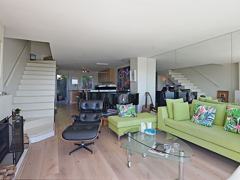 Spacious open-plan living area featuring light hardwood flooring, a fireplace, a central staircase, and a large mirrored wall reflecting the kitchen space.