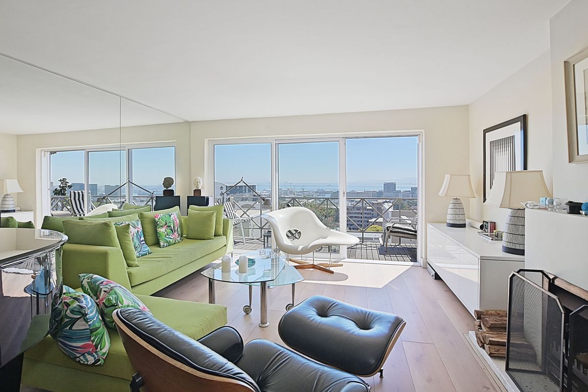 Spacious living room featuring hardwood flooring, a fireplace, and large sliding glass doors that open to a balcony with expansive city and ocean views.