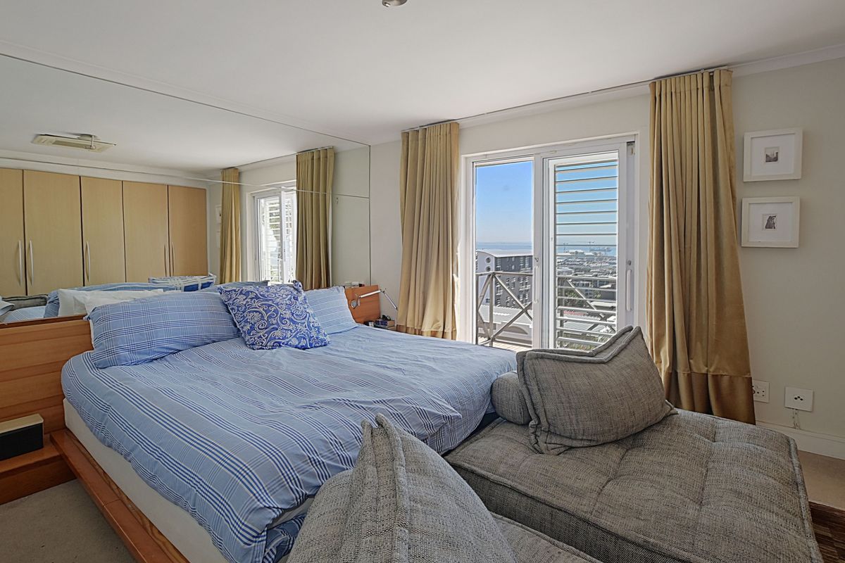 A bedroom featuring built-in cupboards, a mirrored wall, and a sliding glass door leading to a balcony with coastal views.