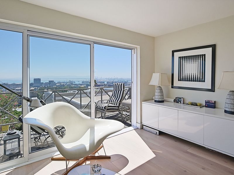 Bright living room featuring large sliding glass doors that open onto a balcony with expansive city and harbor views.