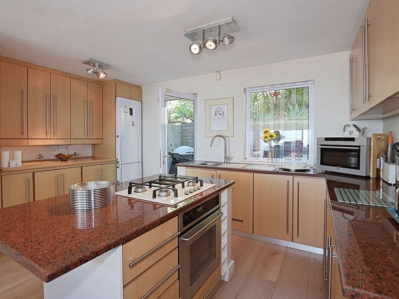 Modern kitchen featuring light wood cabinetry, granite countertops, a central island with a gas hob, and direct access to an outdoor area.