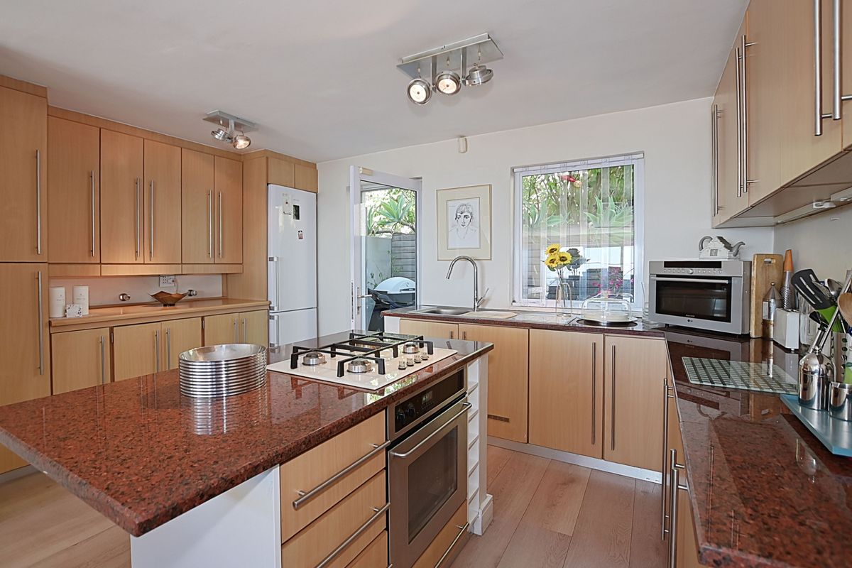 Modern kitchen featuring light wood cabinetry, granite countertops, a central island with a gas hob, and direct access to an outdoor area.