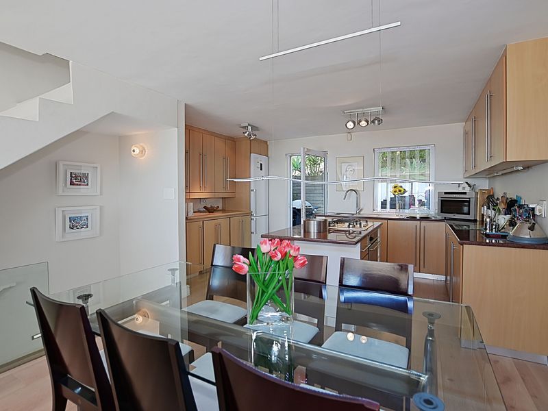 Open-plan kitchen and dining area featuring light wood cabinetry, a central island with a gas hob, and a staircase with a glass balustrade.