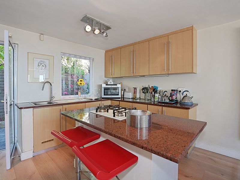A functional kitchen featuring light wood cabinetry, granite countertops, a central island with a gas hob, and direct access to an outdoor patio area.