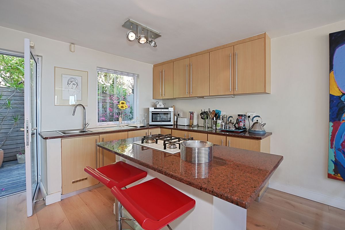 A functional kitchen featuring light wood cabinetry, granite countertops, a central island with a gas hob, and direct access to an outdoor patio area.