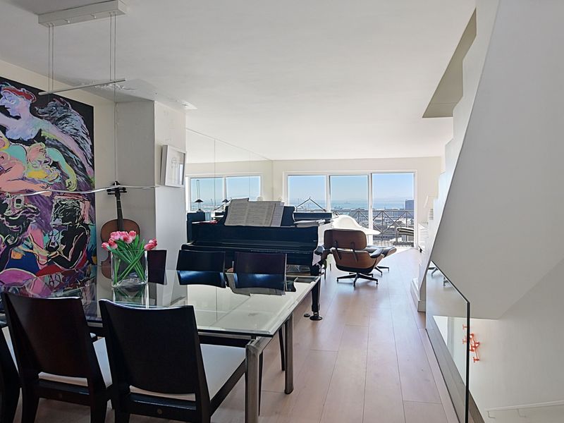 Spacious open-plan living and dining area featuring light hardwood flooring, a modern staircase with glass balustrade, and large sliding doors leading to a balcony.