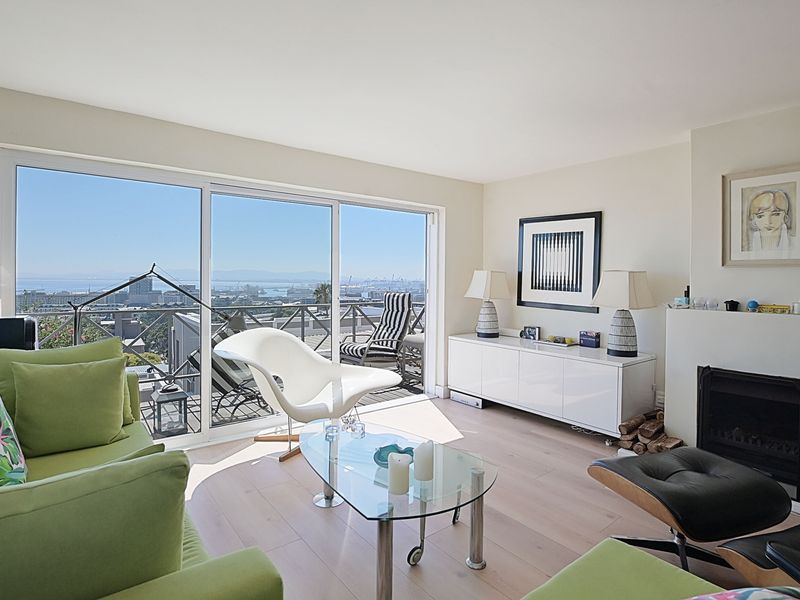 Bright living room featuring hardwood flooring, a fireplace, and large sliding glass doors that open to a balcony with expansive city and ocean views.