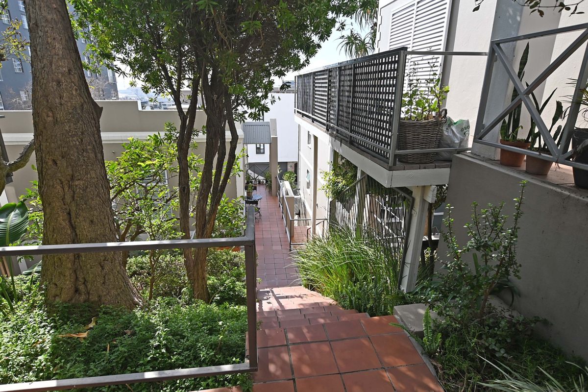 A view of a tiled outdoor staircase leading down through a landscaped garden area, featuring metal railings and an elevated balcony structure.