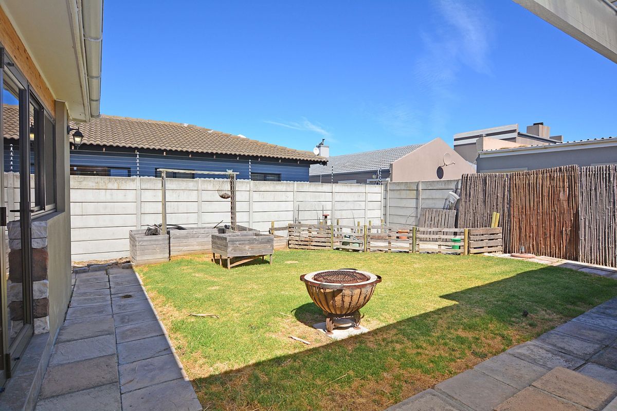 A private rear garden featuring a lawn area, paved patio space, and perimeter walling with security fencing.