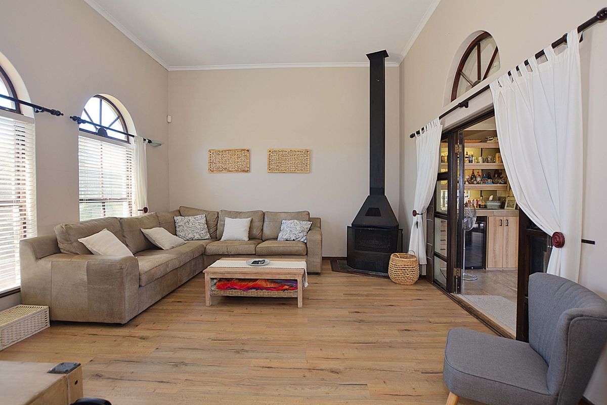 Spacious living room featuring high ceilings, arched windows, wood-look flooring, and a prominent black freestanding fireplace, with an adjacent bar area.