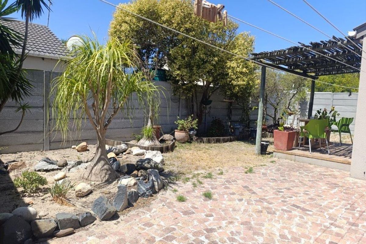 A private rear garden featuring a paved patio area, a wooden pergola, and established landscaping with rock features and boundary walling.
