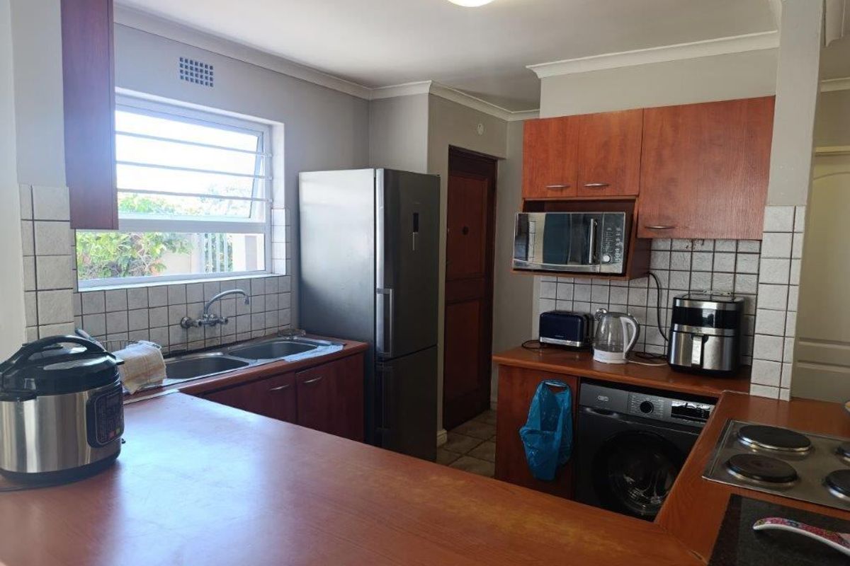 Functional kitchen featuring wood-finish cabinetry, tiled splashbacks, double sink, and integrated hob, offering a practical layout for daily meal preparation.