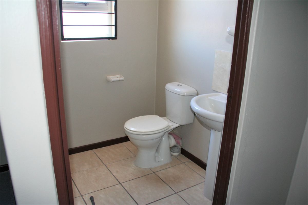 A compact guest bathroom featuring a pedestal basin, standard toilet, tiled flooring, and a small window with security bars.