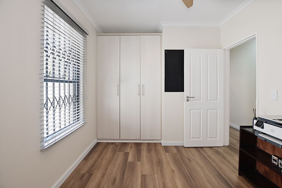 A bright bedroom featuring wood-look flooring, built-in cabinetry, and a window fitted with security bars and blinds.