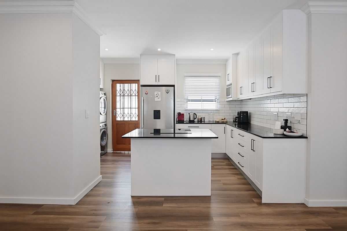 Modern kitchen featuring white cabinetry, black countertops, subway tile backsplash, and a central island, with an adjacent laundry area and exterior door access.