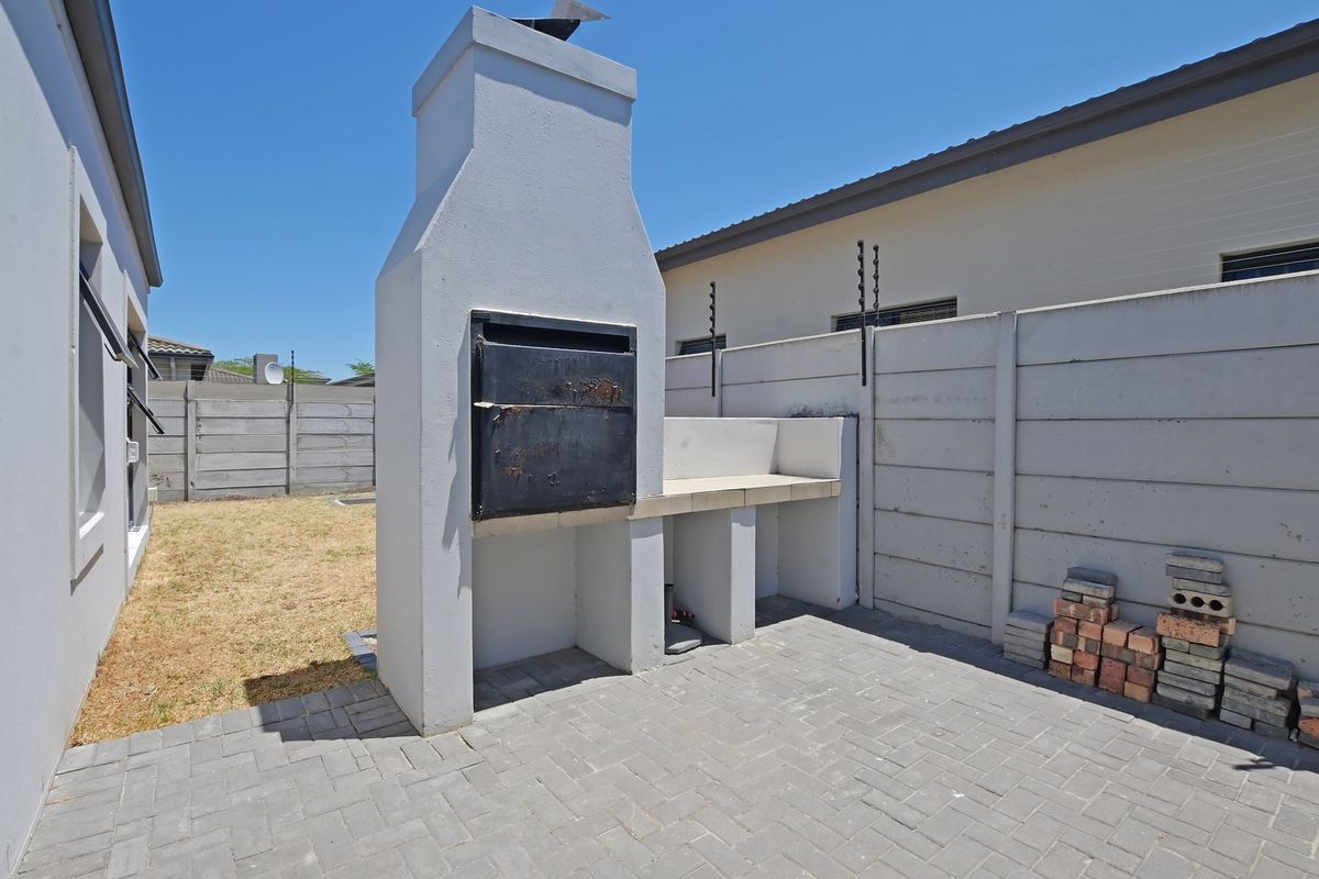 Outdoor patio area featuring a built-in masonry braai and paved flooring, set within a private rear garden with perimeter walling.