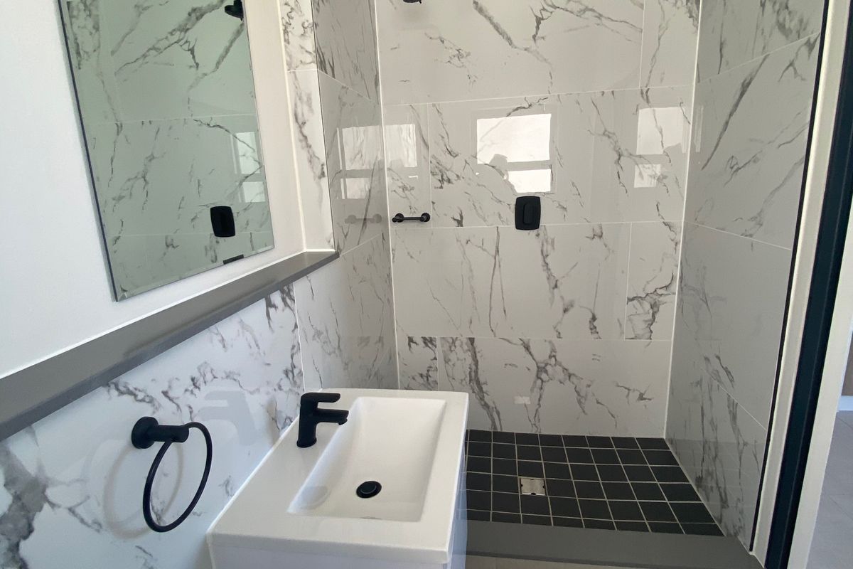 Modern bathroom featuring a walk-in shower with marble-look wall tiles, black fixtures, a wall-mounted vanity, and a sleek mirror.