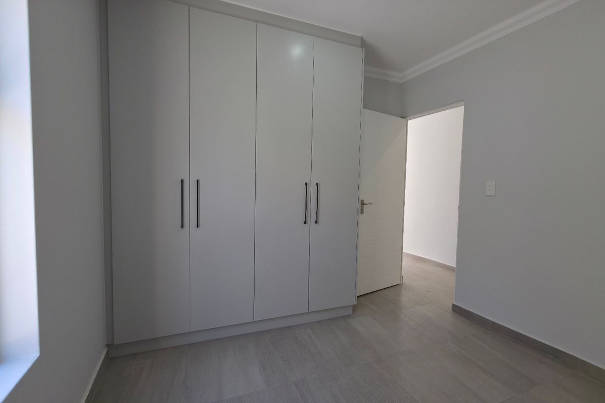 A clean, modern bedroom featuring neutral tiled flooring, built-in white cupboards, and crisp finishes, ready for personalization.