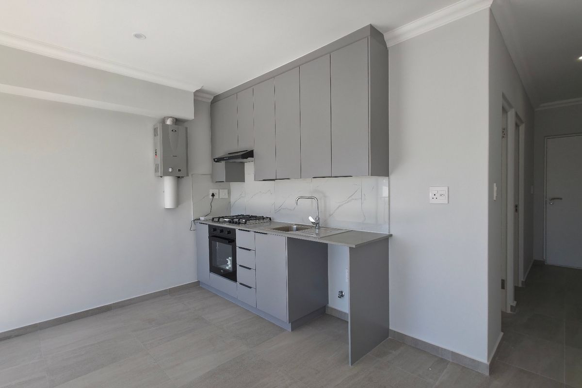 A modern, compact kitchen featuring grey cabinetry, a gas hob, electric oven, and a sleek marble-look splashback in an open-plan apartment setting.