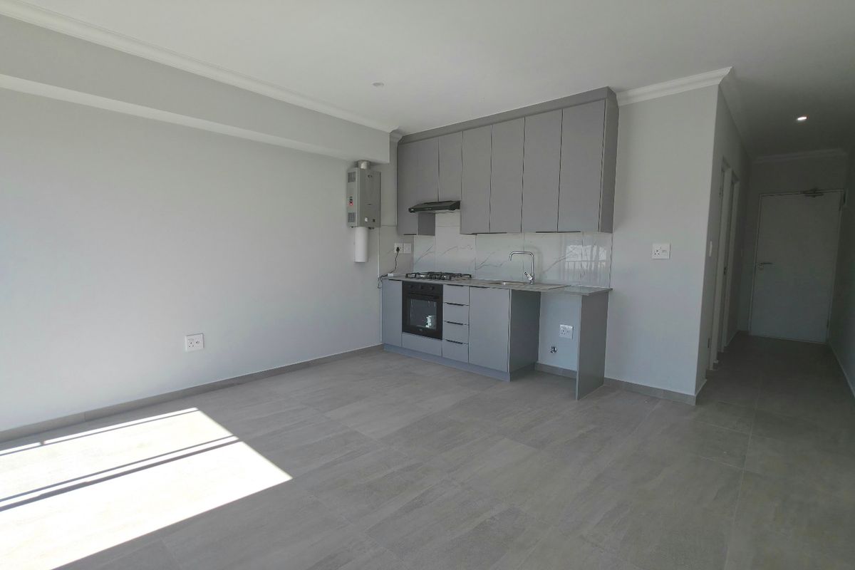 Modern open-plan living area featuring a compact kitchen with built-in cabinetry, gas hob, oven, and stone countertops, finished with neutral tiled flooring.