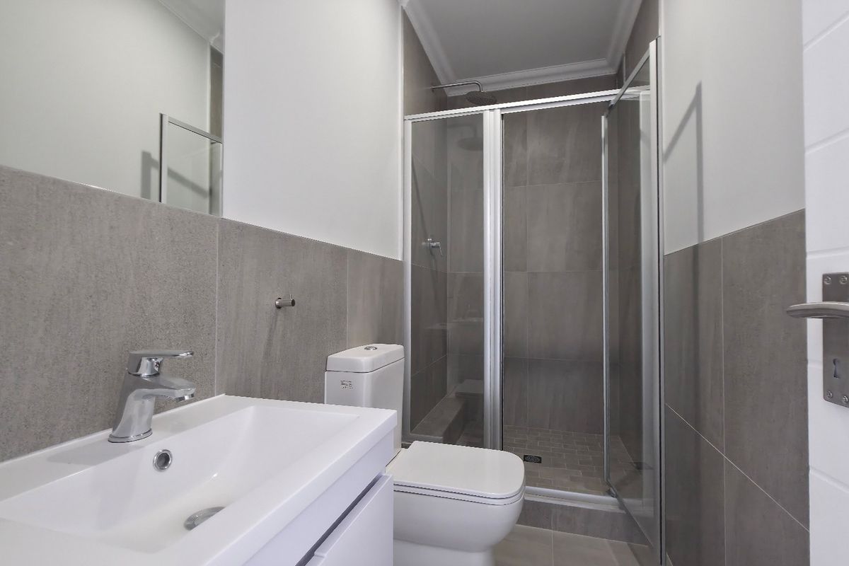 Modern bathroom featuring a sleek vanity basin, toilet, and a glass-enclosed shower with contemporary grey wall and floor tiling.