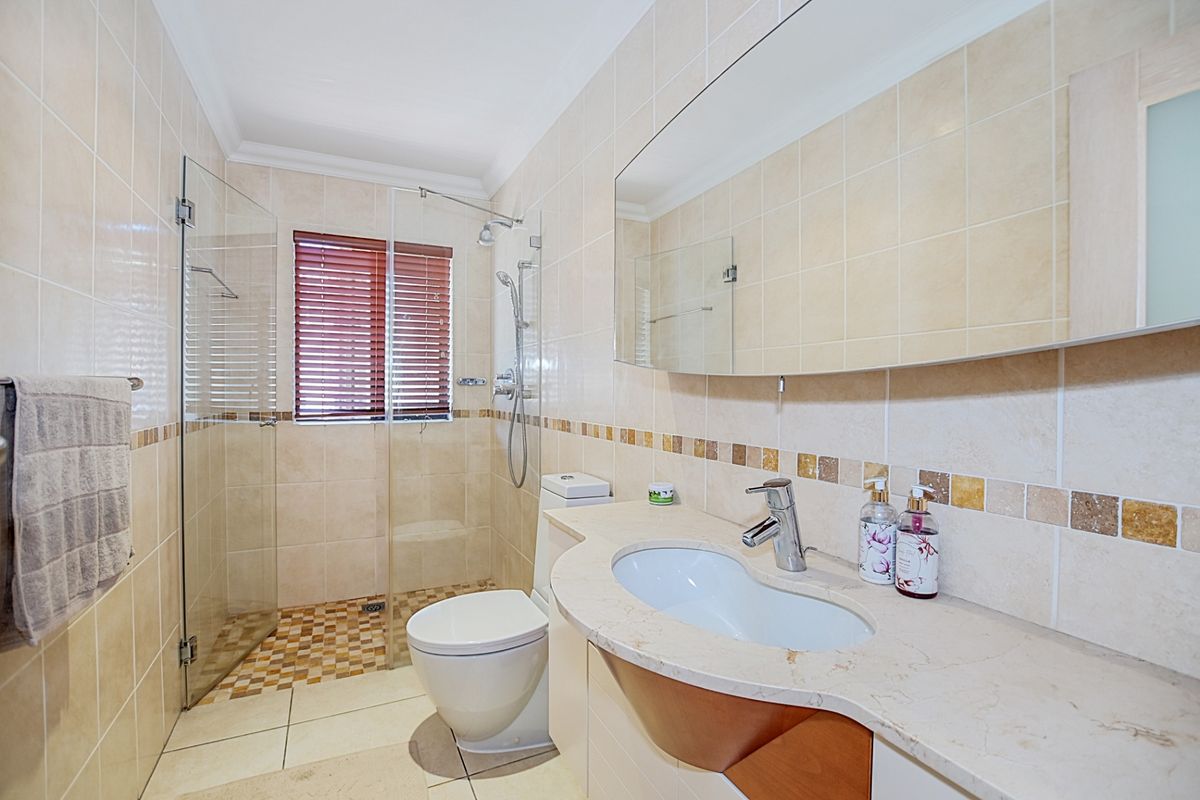 A well-maintained bathroom featuring a glass-enclosed walk-in shower, a modern vanity with a basin, and neutral wall tiling.