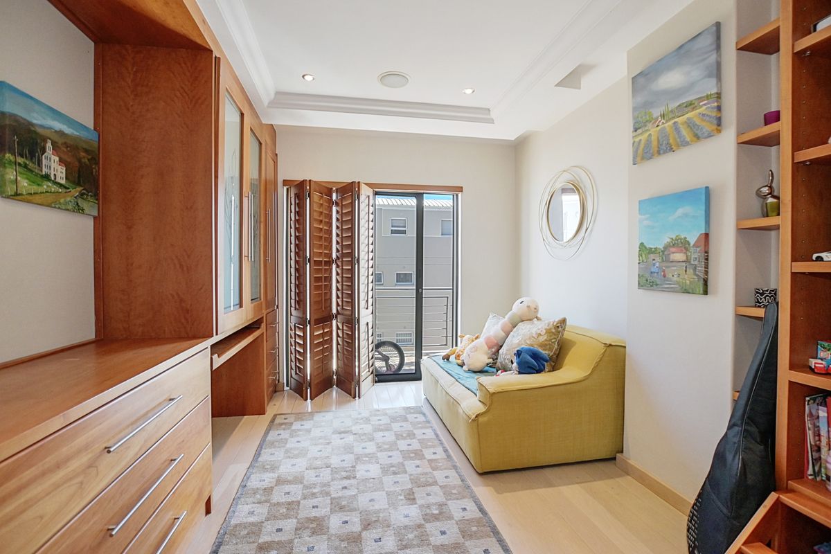 A versatile room featuring extensive built-in wooden cabinetry, shelving, and access to a private balcony through folding shutters.