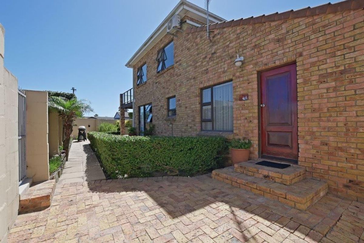 A side view of the brick house featuring a paved walkway, a solid timber entrance door, and established garden hedging.