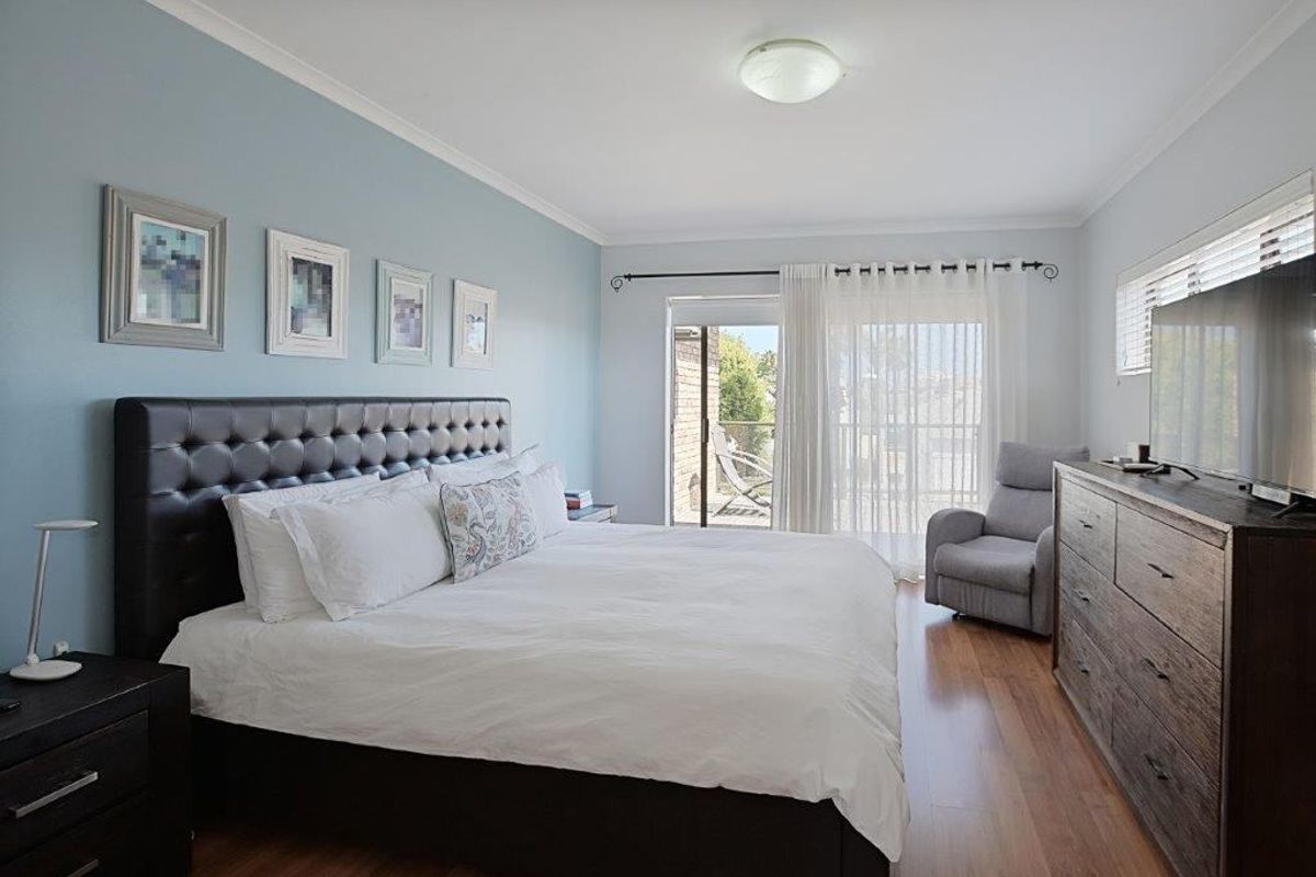 Spacious bedroom featuring light blue accent wall, laminate flooring, and sliding glass door access to a private balcony.
