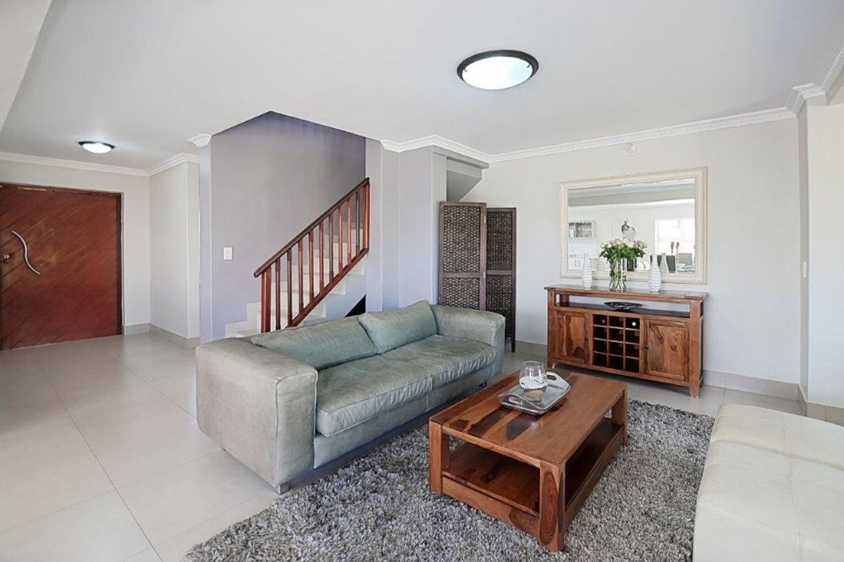 Spacious living area featuring tiled flooring, crown molding, and a wooden staircase with a matching balustrade, creating a welcoming and open atmosphere.