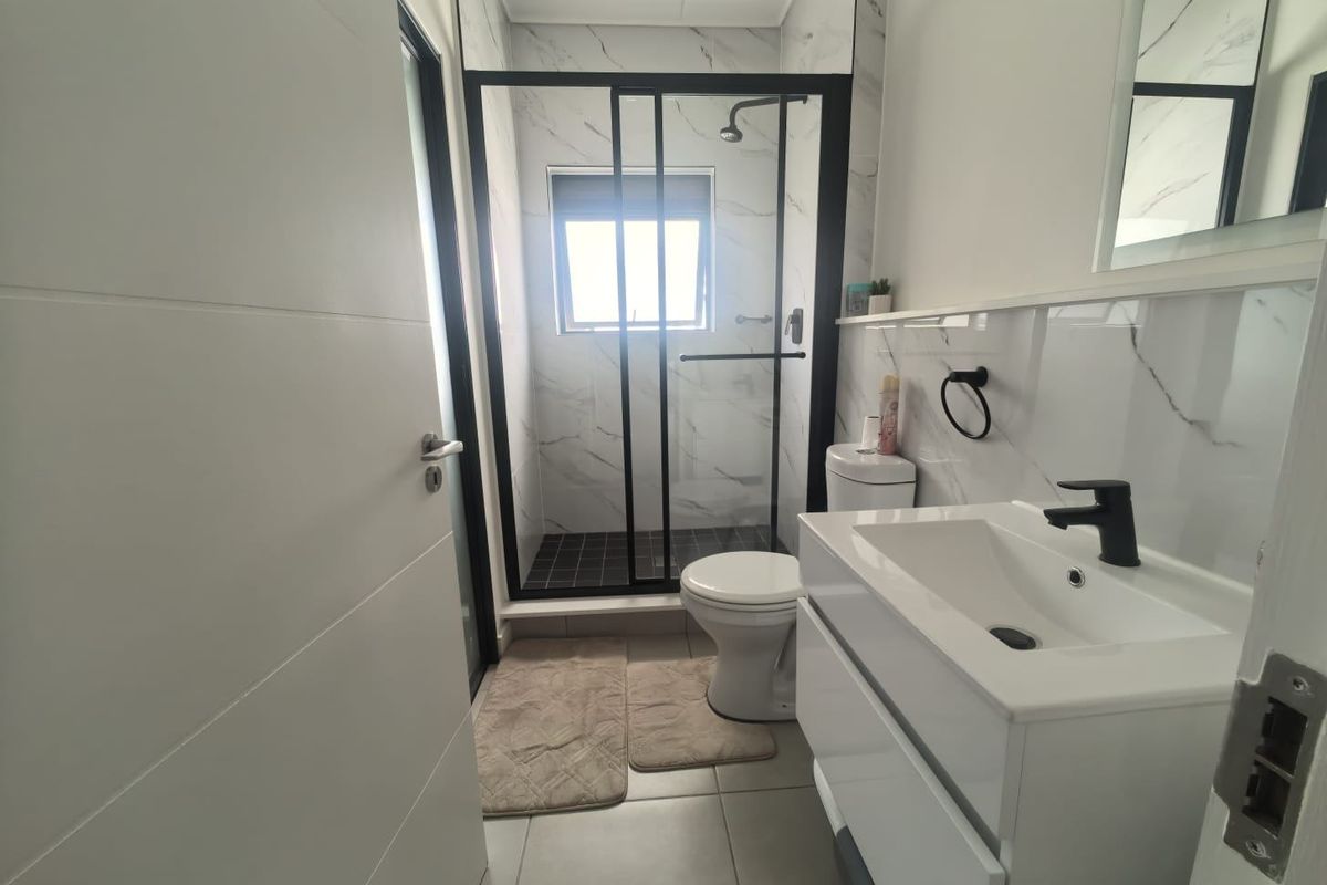Modern bathroom featuring a glass-enclosed shower with black frame, marble-look wall tiles, a contemporary vanity with black faucet, and a white toilet.