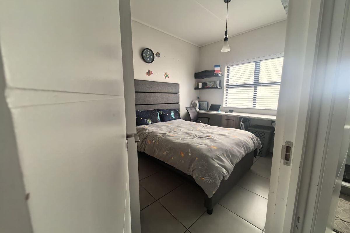 A functional bedroom featuring tiled flooring, a built-in desk area, and a window with fitted blinds, offering a practical living space.